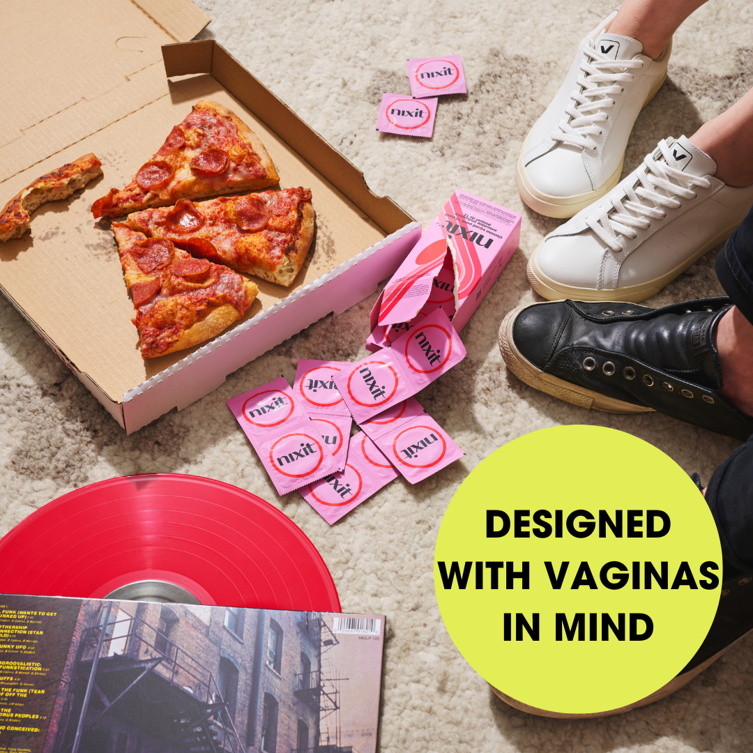 An open pizza box is between two pairs of feet and a ripped open box of nixit condoms.  Wording in a circle reads 'Designed with vaginas in mind'.