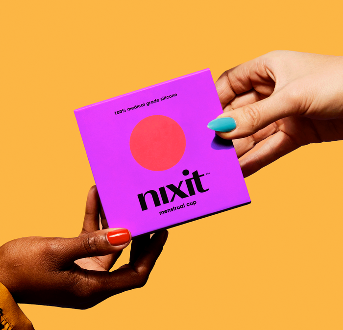 Hands holding a nixit menstrual cup box with colorful painted nails against an orange background.