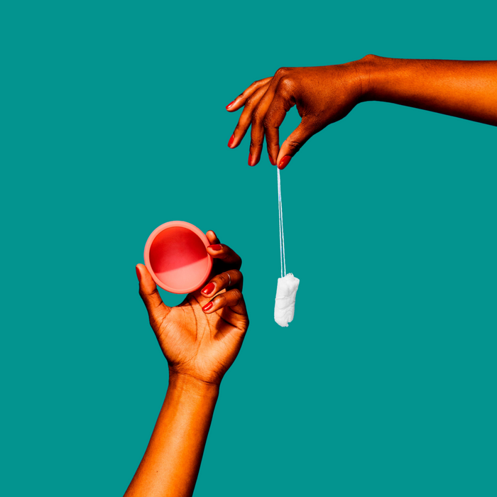 Two hands holding a menstrual cup and tampon against a teal background.